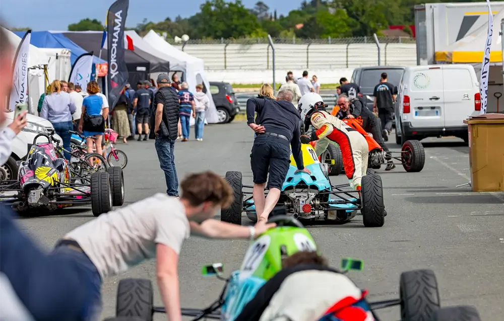 Jeunes pilotes en monoplace dans les paddocks, accompagnés par les équipes techniques avant la mise en grille de départ sur circuit